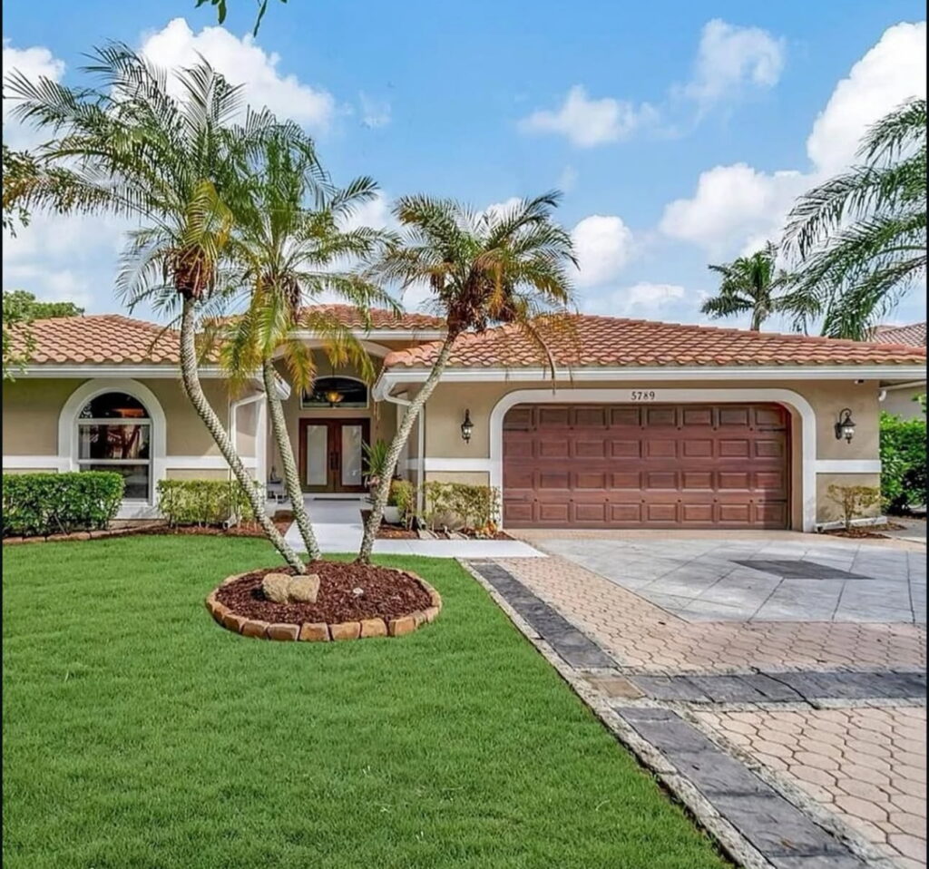 Front exterior of a single-story home with a tile roof replacement in Coconut Creek, Florida featuring a paver driveway and tropical landscaping